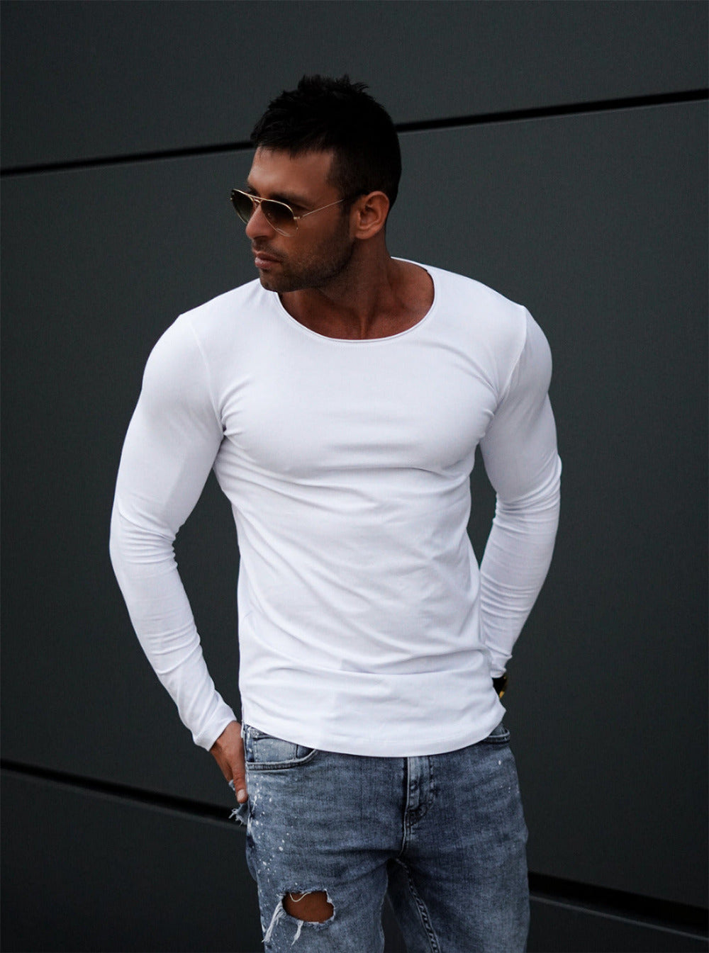 Man wearing a white long-sleeve shirt and ripped jeans against a dark background