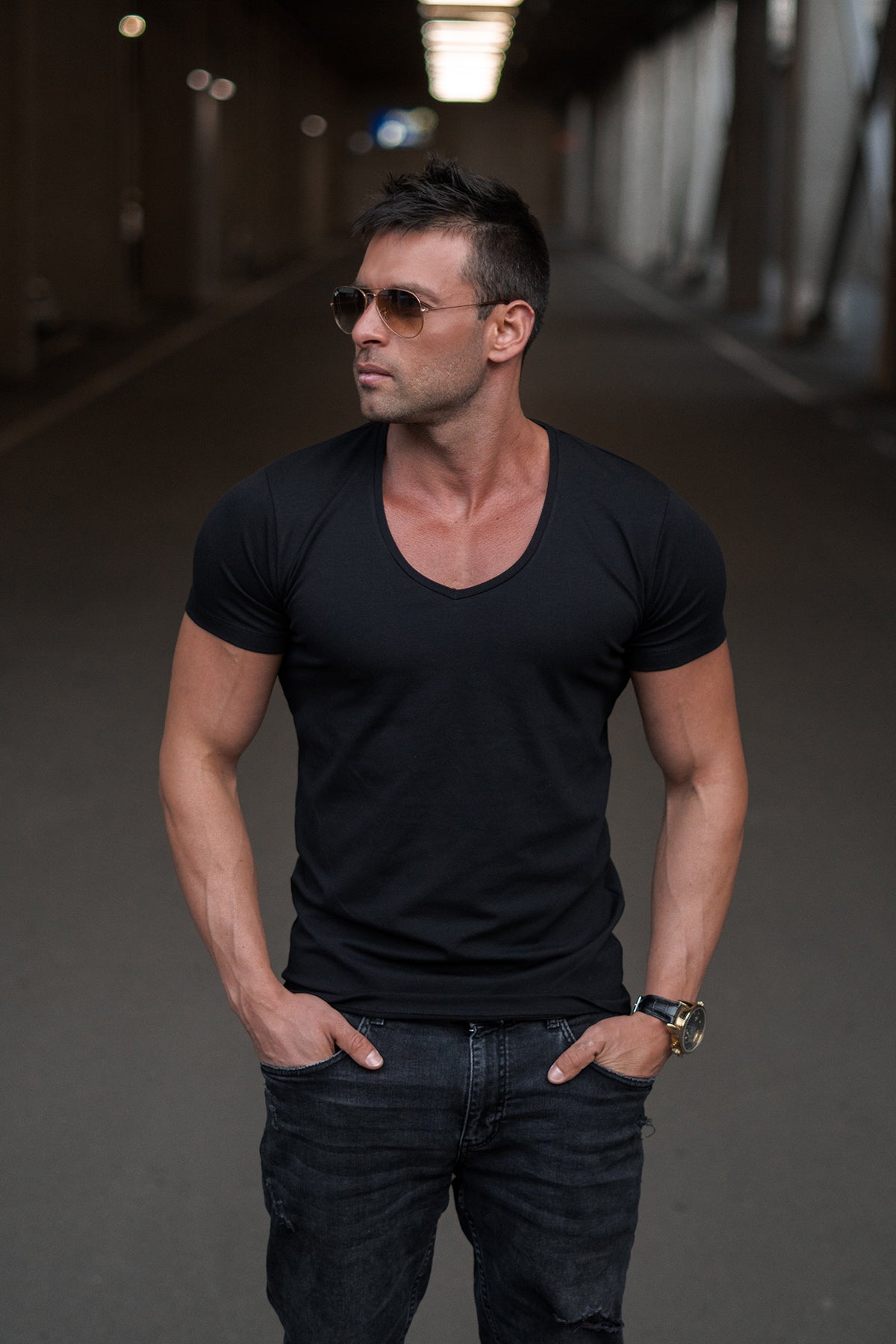 Man wearing a black deep V-neck t-shirt and sunglasses in an urban setting